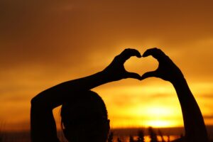 A silhouette of a person forming a heart shape with hands against a stunning sunset.